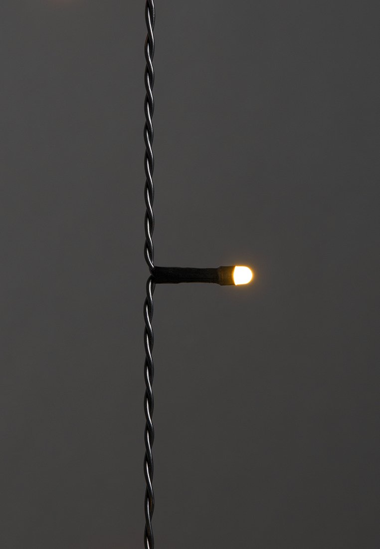 Eine einzelne warmweiße LED-Lampe auf einem gedrehten schwarzen Draht vor dunklem Hintergrund, beleuchtet und vertikal hängend.