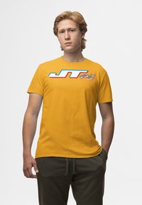 Gul bomulds T-shirt med et hvidt og rødt "JT Racing" grafisk tryk. Korte ærmer, rund hals, afslappet pasform. Enkel, glat tekstur.