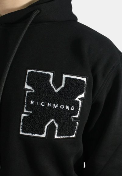 Felpa nera con cappuccio caratterizzata da un grande logo "X" in bianco e nero testurizzato, con la parola "RICHMOND" in bianco, su uno sfondo di tessuto liscio.
