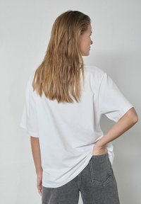 Balta pārmērīga lieluma T-krekls īsām piedurknēm, glāns kokvilnas audums, kopā ar augsta vidukļa pelēkamiem džinsa biksēm ar aizmugures kabatu.