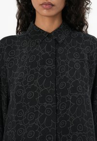 Schwarzes Hemd mit floralem Muster und grauen Konturen, mit Knopfkragen und glattem, strukturiertem Stoff.
