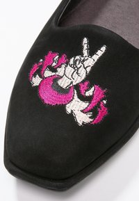 Scarpa flat nera in suede con punta affusolata caratterizzata da un vibrante motivo ricamato di un simbolo della pace in rosa e bianco. Texture morbida e stile minimalista.