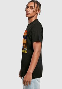 Sort T-shirt med rund hals, med et farverigt trykt design af en muskuløs figur på fronten. Blødt bomuldsstof.