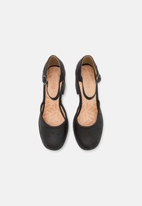 Černé kožené boty s uzavřenou špičkou, nastavitelným páskem a otevřenými stranami. Mají texturovanou stélku se vzorem listu. Nízký podpatek.