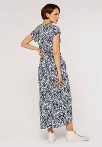 Maxikleid in Weiß und Marineblau mit einem Wellenmuster, kurzen Ärmeln, tailliertem Schnitt und ausgestelltem Rock, kombiniert mit weißen High-Top-Sneakern.