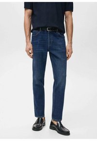 Vaqueros de mezclilla azul oscuro con corte de pierna recta, que cuentan con cinco bolsillos, costuras sutiles y trabillas para cinturón. Combinados con mocasines negros.