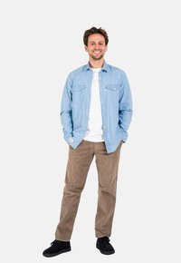 Helles blaues Button-Down-Hemd über einem weißen T-Shirt, kombiniert mit beigem Cordhosen und schwarzen Schuhen. Glatter Stoff, normale Passform, zwei Brusttaschen.
