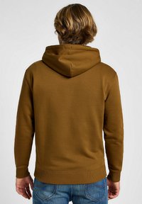 Felpa marrone con cappuccio regolabile, polsini e orlo a coste. Realizzata in un materiale morbido e testurizzato. Modello mostrato di spalle.