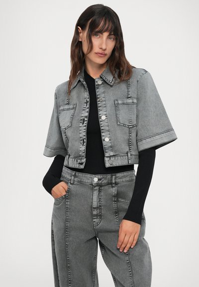 Kvinne med grå cropped denimjakke med store lommer og matchende grå høyt midje jeans, svart ribbestrikket langermet topp under.