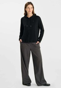 Zwarte hoodie met knoopsluiting, trekkoordkap en lange mouwen, gecombineerd met grijze streepjes brede broek. Beide materialen hebben een zachte textuur.