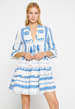 Vestido blanco con patrones geométricos azules, con escote en V, mangas tres cuartos y una falda de volantes con detalles de borlas.