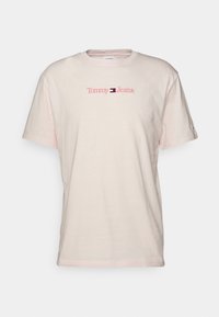 Camiseta de algodón color beige claro con mangas cortas. Presenta el logo de "Tommy Jeans" en rosa en el pecho. Cuello redondo clásico.