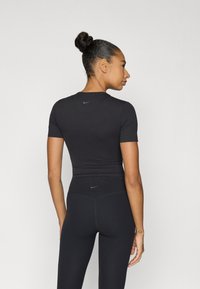 Μαύρο αθλητικό τοπ με κοντά μανίκια, εφαρμοστή σχεδίαση. Το υλικό φαίνεται λείο με ένα μικρό μπλε λογότυπο Nike κοντά στον γιακά.