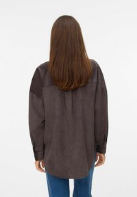 Donkere, bruin, lange mouwen shirt gemaakt van zachte stof, met een ontspannen pasvorm, achterpand naad en knoopmanchetten. Draag het met blauwe jeans.