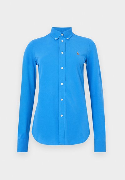 Modrá košeľa s dlhými rukávmi a golierom na gombíky, vybavená bielymi gombíkmi a malým vyšitým logom na ľavej strane hrude. Hladká textúra látky.