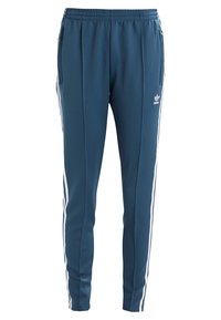 Blå sportbyxor med vita sidostripes, elastisk midja och två sidfickor; tillverkade av slät, lätt tyg. Adidas-logotyp framtill.