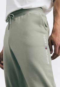 Lys grønne træningsbukser lavet af blødt materiale med elastisk talje, sidelommer og hvid broderet "TOMMY HILFIGER" branding.