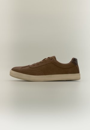 Bruine suède lage sneaker met beige zool en donkerbruine hielpatch, weergegeven op een effen lichte achtergrond.