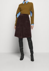 Ruskea corduroy-rypistys hame, yhdistettynä ribattuun sinappikeltaiseen neuleeseen ja siniseen kauluspaitaan. Mustat polven ylle ulottuvat korkokengät täydentävät asukokonaisuuden.