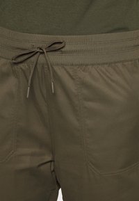 Shorts vert olive avec taille élastique et cordon de serrage. Présente des détails cousus et une texture lisse. Poches sur les côtés.