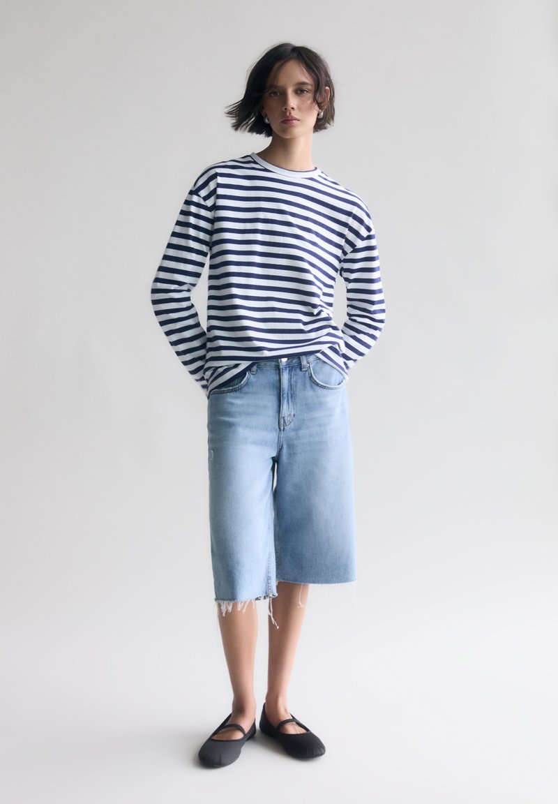 Maglietta a righe blu navy e bianche a maniche lunghe, pantaloni corti in denim azzurro chiaro e scarpe nere senza tacco. Design semplice e casual con una vestibilità rilassata.