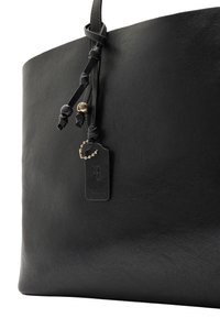Czarna skórzana torba typu tote o gładkiej fakturze, z węzłowymi akcentami ze skóry, suwakiem oraz małą metką przymocowaną łańcuszkiem.