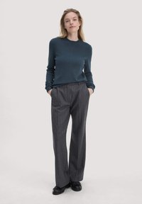 Donker teal crewneck trui met lange mouwen, gecombineerd met grijze streepjesbroek en zwarte instapschoenen.