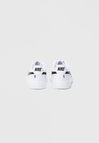 Biele tenisky značky Nike s hladkou textúrou a čiernym zdobným pásikom. Majú polstrovaný golier a detail loga na zadnej strane.