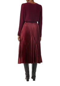 Bordowy longsleeve zestawiony z plisowaną, wysoką spódnicą, wykonana z błyszczącego materiału. Czarne kozaki za kolano dopełniają stylizację.