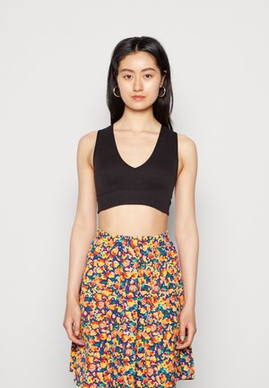 Top cropped preto com um design em V, combinado com uma saia estampada floral com flores vibrantes laranja e rosa sobre um fundo escuro.