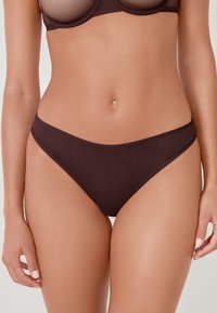 Bas de bikini marron en tissu lisse. Présente un design taille basse avec des côtés étroits et une couverture minimale, sans matériel ni motifs visibles.