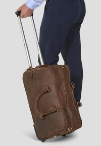 Kahvan nahkainen pyörällinen duffel-laukku, jossa on hopeinen teleskooppikahva, sivukahvat, vetoketjusulku ja kultaisentynkäiset koristelut.
