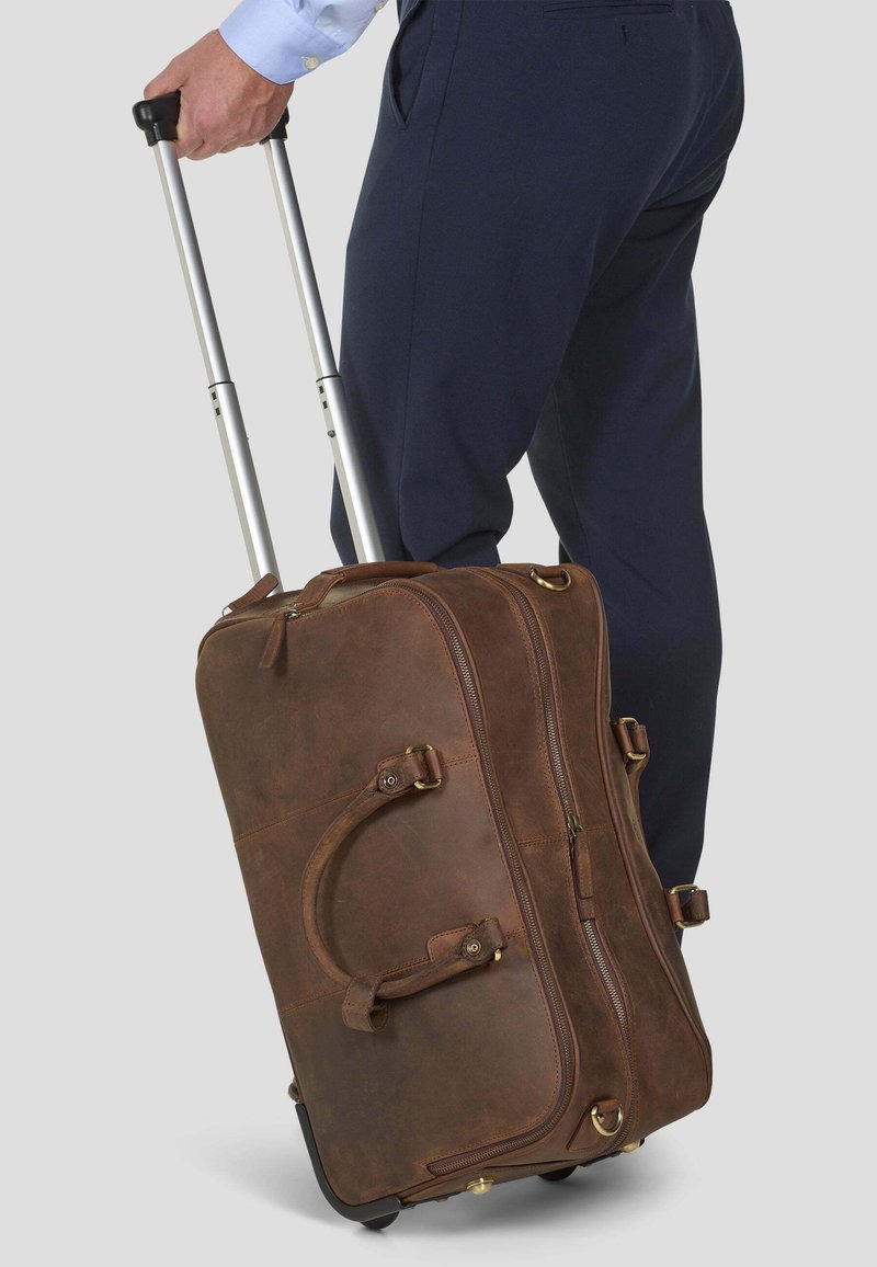 Kahvan nahkainen pyörällinen duffel-laukku, jossa on hopeinen teleskooppikahva, sivukahvat, vetoketjusulku ja kultaisentynkäiset koristelut.