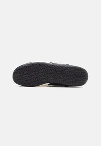 Must must sneaker põhja mustast kummist, millel on mustrit ja valget aktsenti. Omab siledat tekstuuri ja logo muljet.