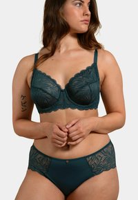 Soutien-gorge en dentelle teal avec armatures et bords festonnés, associé à un brief assorti en dentelle teal. Matériau lisse et détails en motif de feuilles.