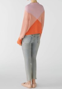 Gebreide trui met diagonale kleurvlakken in roze, perzik en oranje; ontspannen pasvorm met geribbelde manchetten, gecombineerd met lichtblauwe skinny jeans en lichte schoenen.