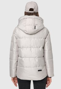 Ljusgrå puffjacka med huva, med horisontell quiltad sömnad och ett logotypmärke. Matchas med en lika färgad keps.