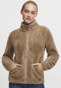 Brown fleece jacket with high collar, front zipper, side pockets, and textured fabric. Designed for warmth and comfort.