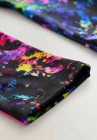 Flerfärgat tyg med en svart botten som har livfulla inslag av rosa, gult, blått och grönt. Mjuk textur och synlig detalj av vikt kant.