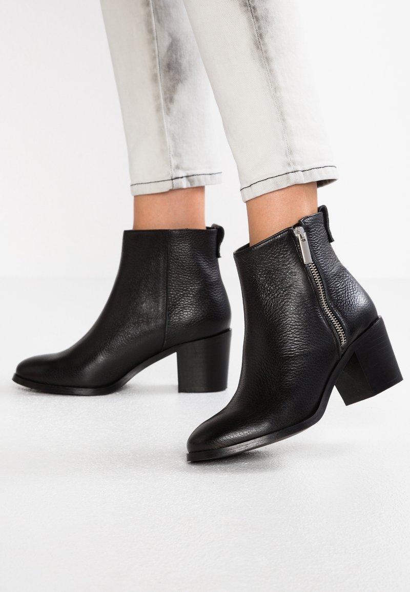 Stivali alla caviglia in pelle nera con una finitura strutturata, dotati di una cerniera laterale e una punta arrotondata, montati su un tacco a blocco.