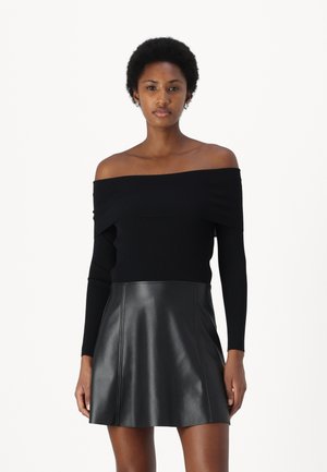 Top nero a spalla scoperta in maglia a costine e gonna corta in pelle nera. Il top ha maniche lunghe; la gonna presenta dettagli di cuciture sottili.