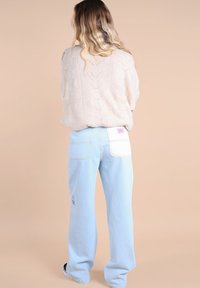 Jean large bleu clair avec une poche à patch et un détail floral brodé, associé à un pull crème en tricot torsadé.