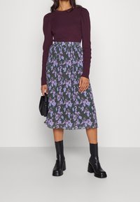 Burgundyribbad långärmad topp med puffärmar, matchad med en golvlång blommig kjol i mörkgrön och lila, samt svarta klackstövlar.