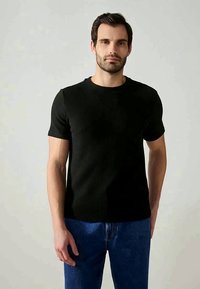 T-shirt preto com nervuras, de manga curta e decote redondo. Usado com jeans de ganga azuis. Textura suave, design ajustado.