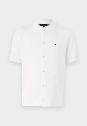 Weißes Polo-Shirt mit kurzen Ärmeln aus einem gestrickten Stoff, mit klassischem Kragen, Knopfverschluss und kleinem Logo auf der linken Brust.