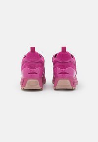 Chaussures de sport roses avec une tige en mesh et daim, une languette à l'arrière, et une semelle en caoutchouc texturée. Détail du logo à l'arrière.