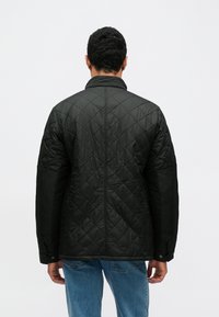 Czarna pikowana kurtka z wysokim kołnierzem, ozdobionym wzorem i zapięciami na zatrzaski na rękawach. Połączona z jasnoniebieskimi jeansami.