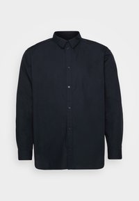 Chemise noire à manches longues avec boutons, col pointu et poignets boutonnés, présentée sur un fond gris clair uni.
