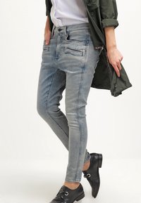 Bledé modré skinny džíny s hladkou texturou, obsahující přední kapsy a prošívané detaily, zkombinované s černými botami.