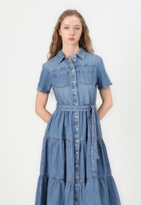 Robe en denim à manches courtes, col chemise, deux poches poitrine, fermeture à boutons sur le devant et ceinture nouée à la taille. Design de jupe évasée en plusieurs niveaux.
